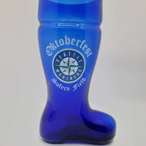May include: A blue glass boot-shaped beer stein with a white "Oktoberfest" inscription and a Seattle Mariners logo. The logo features a compass with a baseball inside and the words "Seattle Mariners Safeco Field".