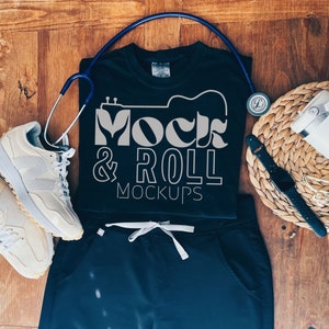 May include: Black t-shirt with the text "Mock & Roll Mockups" in white. The t-shirt is laid flat on a wooden surface with a stethoscope, a watch, a water bottle, and a pair of white sneakers.