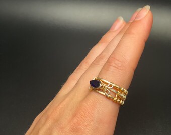 May include: A gold wire wrapped ring with a dark blue gemstone. The ring is worn on a person's finger.