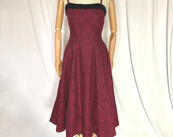 May include: A burgundy sleeveless dress with a black velvet waistband and a paisley pattern.