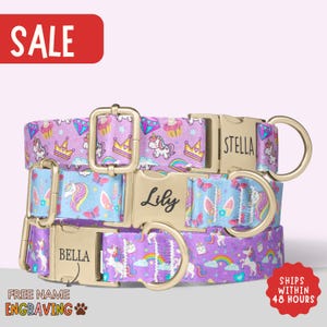May include: Three personalized dog collars with gold-colored buckles. The collars feature a unicorn and rainbow pattern in purple and blue. The names "Bella", "Lily", and "Stella" are engraved on the buckles. The word "SALE" is in a red box.
