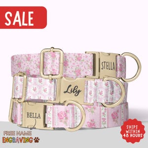 May include: Three pink floral dog collars with gold-colored hardware. Each collar has a different name engraved on the buckle: Lily, Stella, and Bella. The image includes the text "SALE" and "FREE NAME ENGRAVING".