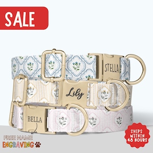 May include: Three patterned dog collars with gold-colored hardware. The collars feature floral and geometric designs in white, blue, and pink. Each collar has a name engraved on the buckle: "Stella", "Lily", and "Bella". The word "SALE" is in a red rectangle.