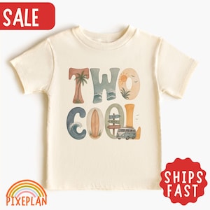以下が含まれることがあります： クリーム色の半袖Tシャツで、大きなスタイリッシュな文字で「TWO COOL」と書かれています。グラフィックには、ヤシの木、海の波、サーフボード、太陽、鳥、木製の標識、ヴィンテージのキャンピングカーのイラストが描かれています。