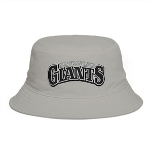 May include: A light gray bucket hat with the text "SAN FRANCISCO GIANTS" in black and white. The hat has a rounded crown and a downward-sloping brim. The text is in a bold, stylized font.