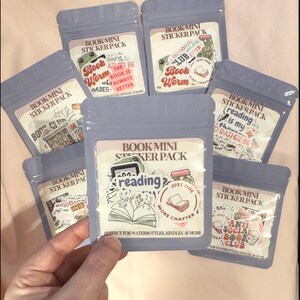 May include: Eight small clear plastic bags with colorful stickers inside. Each bag has a label that says "Book Mini Sticker Pack" and features a different book-themed design. The stickers are perfect for water bottles, Kindles, and more.