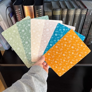 May include: A set of six rectangular bookmarks arranged in a fan shape, each featuring a white botanical line art pattern. The colors include light green, sage green, cream, pale pink, teal, and mustard yellow, all with rounded corners.