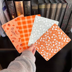May include: Four rectangular bookmarks featuring distinct patterns: one with orange acorns and leaves on a light background, one with an orange and white gingham check, one with white floral motifs on a sage green background, and one with white leaves and flowers on an orange background.
