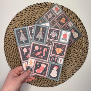 May include: Three pink and gray Christmas-themed cards with a variety of illustrations including a Christmas tree, candy canes, a gingerbread man, a stocking, a snowman, a reindeer, and a sweater. The cards have a postage stamp design with the text "warm wishes" on one card.