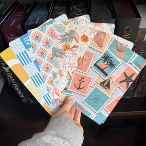 May include: A collection of five rectangular bookmarks featuring various nautical and beach-themed patterns. Designs include blue waves, orange suns, tropical leaves, seashells, and a grid of postage stamp illustrations depicting anchors, sailboats, and starfish.
