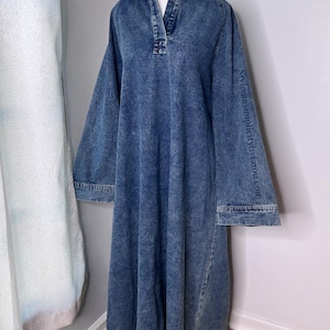 May include: A long-sleeved denim dress with a collared neckline and a button closure. The dress has a relaxed fit and a slightly flared skirt. The dress is a light blue color and has a distressed look.