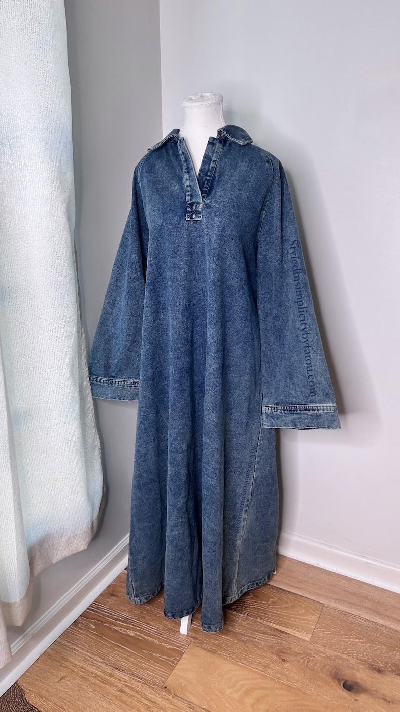 May include: A long-sleeved denim dress with a collared neckline and a button closure. The dress has a relaxed fit and a slightly flared skirt. The dress is a light blue color and has a distressed look.