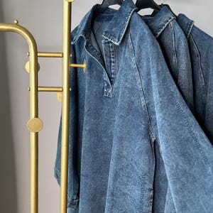 May include: Three denim shirts hanging on a gold metal clothing rack with round accents. The shirts are hanging on black hangers.