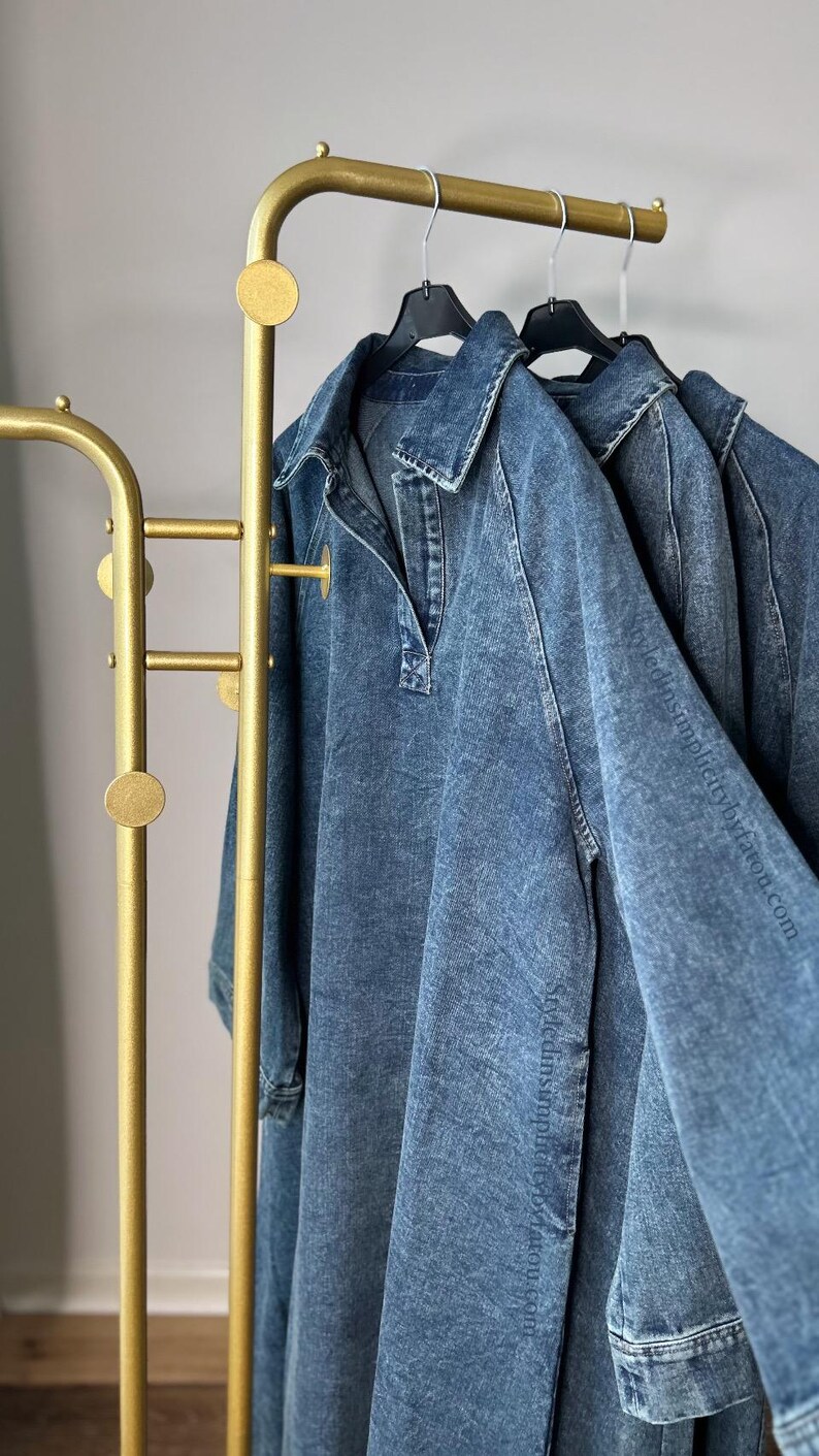 May include: Three denim shirts hanging on a gold metal clothing rack with round accents. The shirts are hanging on black hangers.