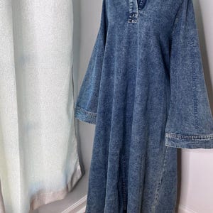 May include: A long, blue denim dress with a collared neckline and long sleeves. The dress has a relaxed fit and a slightly flared skirt.