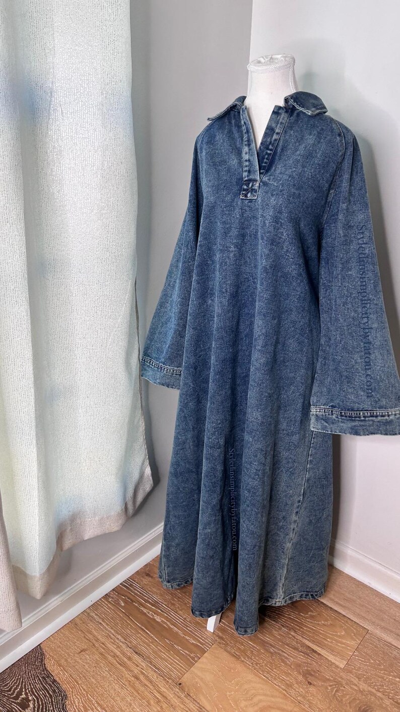 May include: A long, blue denim dress with a collared neckline and long sleeves. The dress has a relaxed fit and a slightly flared skirt.