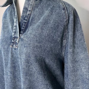 May include: A blue denim shirt with a collared neckline and long sleeves. The shirt has a slightly distressed look and a relaxed fit.