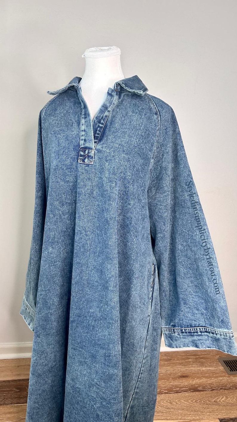 May include: A long-sleeved denim dress with a collared neckline and a button closure. The dress has a relaxed fit and a slightly A-line silhouette. The fabric is a light blue wash with a subtle distressed look.
