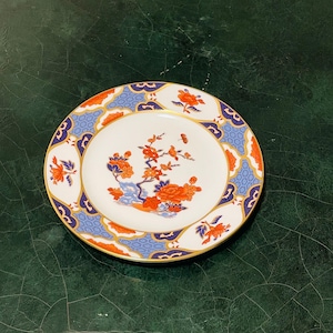 Puede incluir: Un plato de porcelana blanca con un borde azul y dorado y un diseño floral en tonos naranja y rojo.