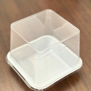 May include: A clear plastic square container with a white lid. The container is empty and has a smooth surface.