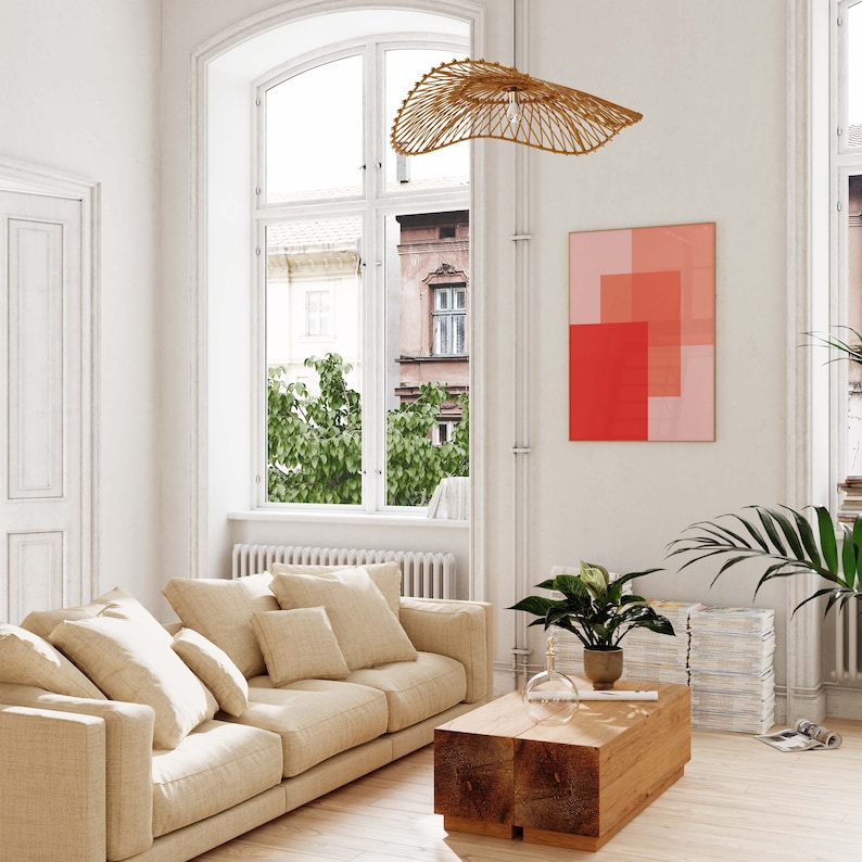 May include: A living room with a beige sofa, a wooden coffee table, and a modern light fixture. A framed artwork with red and pink geometric shapes hangs on the wall. A large window offers a view of the outside.