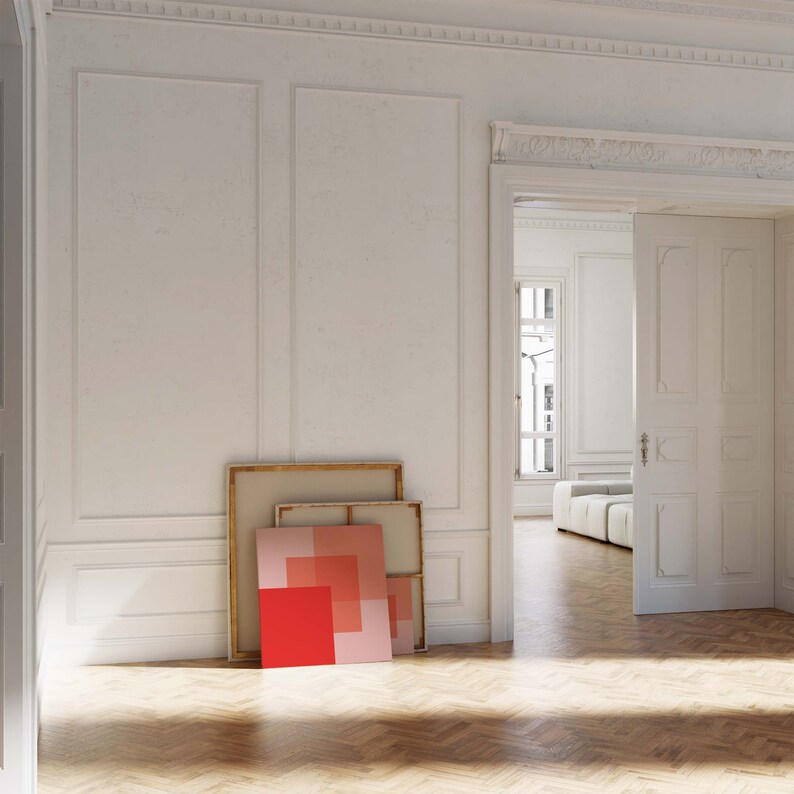 May include: An interior shot of a room with white walls, a wooden floor, and an open doorway. Leaning against the wall are framed artworks with red and pink geometric designs. The room has a classic, elegant aesthetic.
