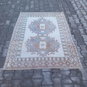 May include: A vintage rug with a cream background and a geometric pattern in shades of blue, pink, and brown. The rug has a fringed edge.