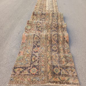 Puede incluir: Una alfombra vintage larga y estrecha con un patrón descolorido multicolor. La alfombra tiene un fondo marrón con intrincados diseños florales en tonos de rosa, azul y verde. La alfombra está flecos en todos los lados.