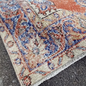 Puede incluir: Una alfombra vintage con fondo crema y patrones intrincados en tonos azules, rojos y naranjas. La alfombra tiene un borde con flecos y está doblada por la mitad.