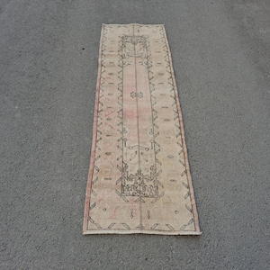 Könnte beinhalten: Ein rechteckiger Teppich im Vintage-Stil mit zentralem Design und Bordüre. Der Teppich hat eine verblasste rosa-beige Farbpalette mit komplizierten Mustern in Schwarz. Der Teppich liegt auf einer grauen Oberfläche.