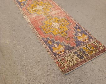 May include: A rectangular, vintage-style rug with a distressed appearance. The rug features a central design in yellow and cream, set against a faded red background. Blue and cream borders frame the design, creating a classic, aged aesthetic.