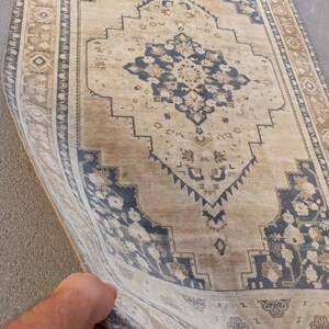 May include: A rectangular, vintage-style rug with a central medallion design. The rug features a beige background with navy blue and brown geometric patterns and floral motifs. The border is a darker shade of brown with repeating geometric shapes.