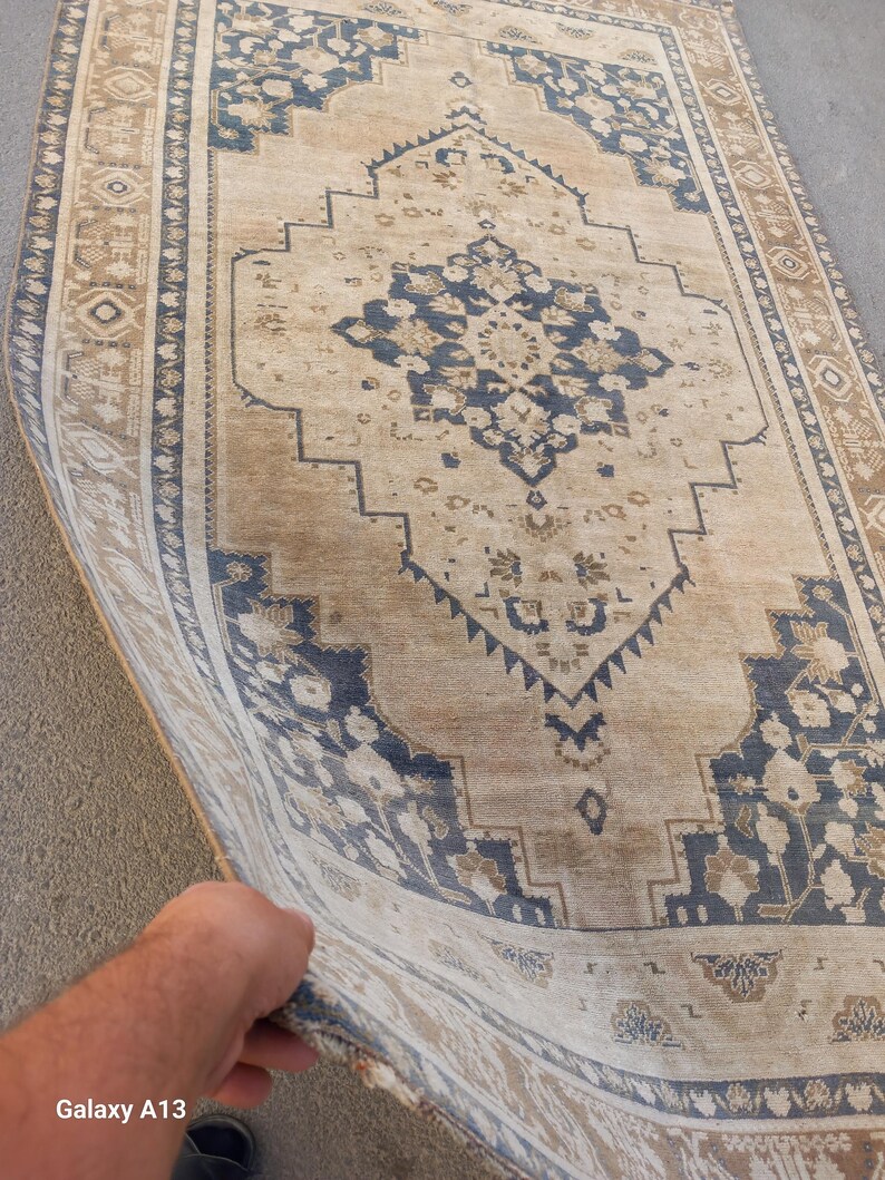 May include: A rectangular, vintage-style rug with a central medallion design. The rug features a beige background with navy blue and brown geometric patterns and floral motifs. The border is a darker shade of brown with repeating geometric shapes.