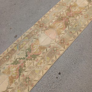 May include: A rectangular, vintage-style rug with a faded, distressed appearance. The rug features a patchwork design with muted colors including beige, brown, pink, and green. Floral and geometric patterns are visible throughout the rug's surface.