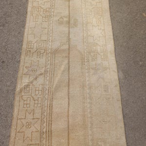 Könnte beinhalten: Ein beigefarbener und hellbrauner Läufer mit geometrischem Bordürendesign. Der Teppich hat ein Mittelfeld mit einem dezenten Muster und einen kontrastierenden Rand mit sich wiederholenden Formen und Linien. Der Teppich ist rechteckig und scheint aus gewebtem Material zu bestehen.