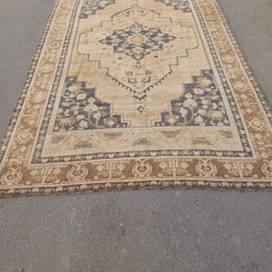 May include: A rectangular, vintage-style rug with a central medallion design. The rug features a beige background with navy blue and brown floral and geometric patterns. The border is a darker brown with repeating motifs.