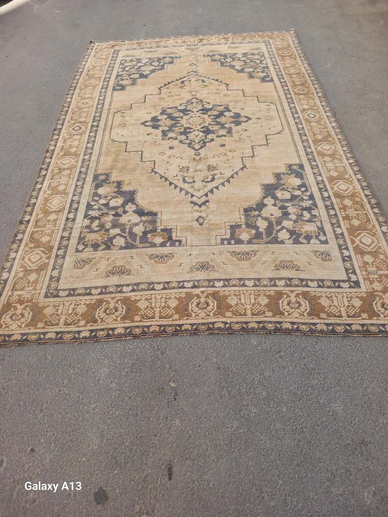 May include: A rectangular, vintage-style rug with a central medallion design. The rug features a beige background with navy blue and brown floral and geometric patterns. The border is a darker brown with repeating motifs.