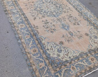 Puede incluir: Una alfombra vintage con fondo beige claro y un patrón floral azul y beige. La alfombra tiene un borde de flecos.