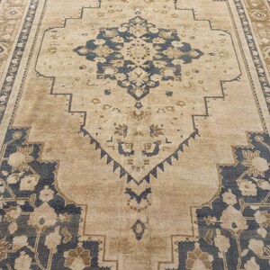 May include: A rectangular area rug with a central medallion design. The rug features a beige background with navy blue and brown geometric and floral patterns. The border has a repeating pattern in brown and beige.