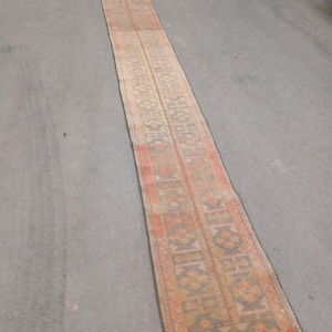 Könnte beinhalten: Ein langer, schmaler, rechteckiger Teppich mit verblichenem, Vintage-Aussehen. Der Teppich weist ein sich wiederholendes geometrisches Muster in Orange, Beige und Grau auf. Die Kanten sind mit einem roten Rand versehen. Der Teppich ist wahrscheinlich aus gewebtem Material.
