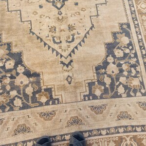 May include: A beige and navy blue patterned rug with a distressed look. The rug features a central medallion design and floral motifs. The border has a repeating pattern. The rug is rectangular and appears to be made of woven material.