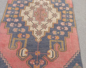 May include: A rectangular, vintage-style rug with a central geometric design. The rug features a salmon-pink field with a navy blue border and central design elements. The design includes floral and geometric patterns in shades of yellow, cream, and pink.