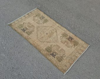 May include: A rectangular beige rug with a central medallion and geometric patterns in shades of brown and green. The rug has a fringed edge and is placed on a gray surface. The rug's design is symmetrical and traditional.