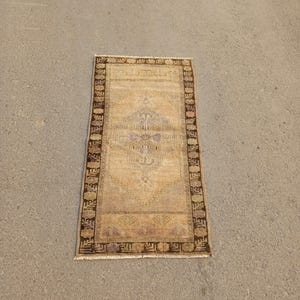 May include: A vintage rug with a beige background and a brown geometric pattern. The rug has a fringe border.