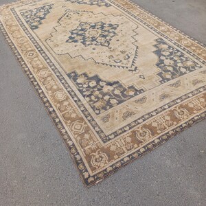 May include: Rectangular beige rug with a central medallion design in navy blue and brown. The rug features an intricate border with floral and geometric patterns, adding a touch of elegance to any room. The rug is likely made of durable materials.