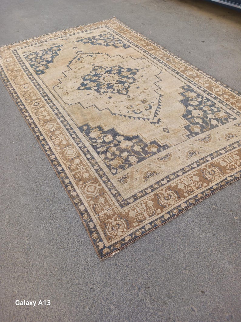 May include: Rectangular beige rug with a central medallion design in navy blue and brown. The rug features an intricate border with floral and geometric patterns, adding a touch of elegance to any room. The rug is likely made of durable materials.