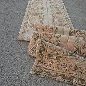 Puede incluir: Varios corredores de alfombras vintage con un aspecto desgastado. Las alfombras presentan una mezcla de tonos beige, rosa y verde oliva con patrones geométricos y florales. Una alfombra está completamente extendida, mientras que otras están parcialmente enrolladas.
