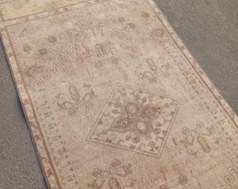 May include: A rectangular, vintage-style rug with a faded, distressed appearance. The rug features a central diamond pattern and floral motifs in shades of beige, red, and brown. The rug is likely made of woven material.
