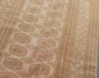 May include: A beige and brown patterned rug featuring a repeating oval design. The rug has vertical stripes along the edges and a central field with the repeating pattern. The rug appears to be made of a woven material.