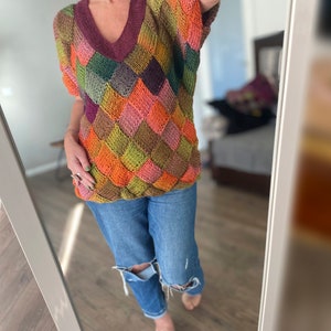 May include: A colourful knitted sweater with a geometric diamond pattern in shades of orange, green, brown, and pink. The sweater has a v-neck and short sleeves.